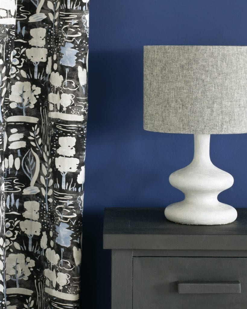 Side table painted with Chalk Paint® in Graphite, a soft charcoal grey black against a wall of Napoleonic Blue. Curtain in Dulcet in Graphite and lampshade in Linen Union in Graphite + Old White