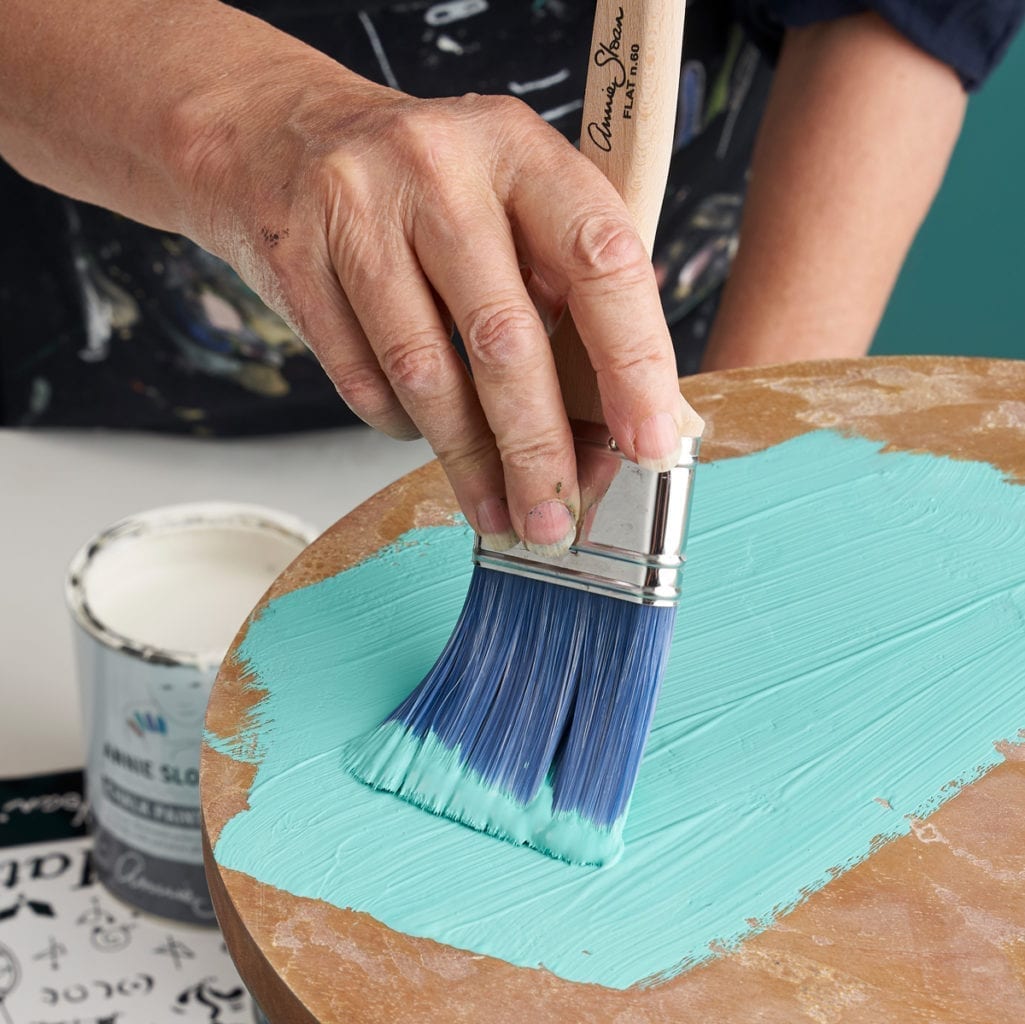 Annie Sloan using Chalk Paint furniture paint in a mix of Florence and OId White to paint a table using a Flat Brush