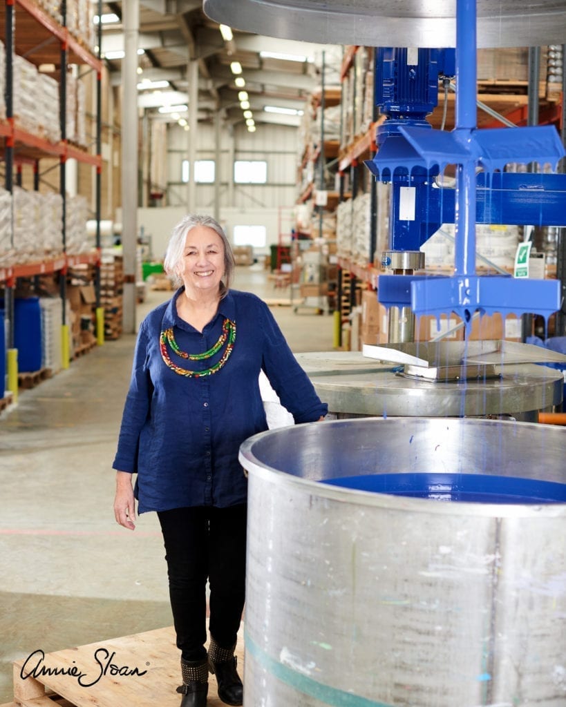 Annie Sloan à côté d’une cuve de peinture Chalk Paint™ en Napoleonic Blue dans son usine à Oxford