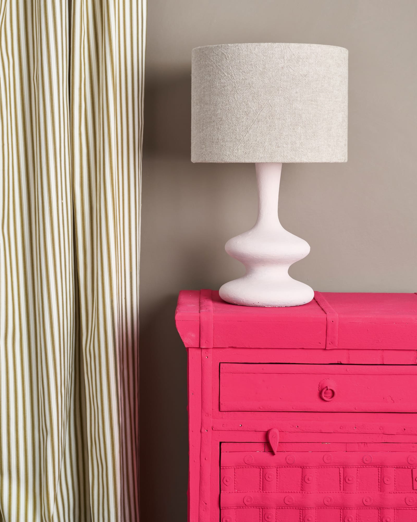 Side table painted with Chalk Paint® in Capri Pink, a bright, hot pink. Curtain in Ticking in Olive fabric and lampshade in Linen Union in Old White + French Linen