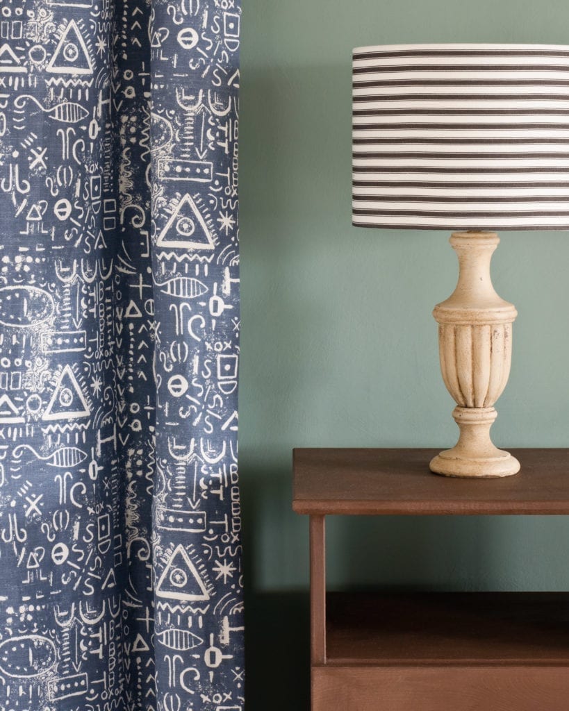 Side table painted with Chalk Paint® in Honfleur, a rich brown against a Duck Egg Blue wall. Curtain in Tacit in Old Violet and lampshade in Ticking in Old Violet