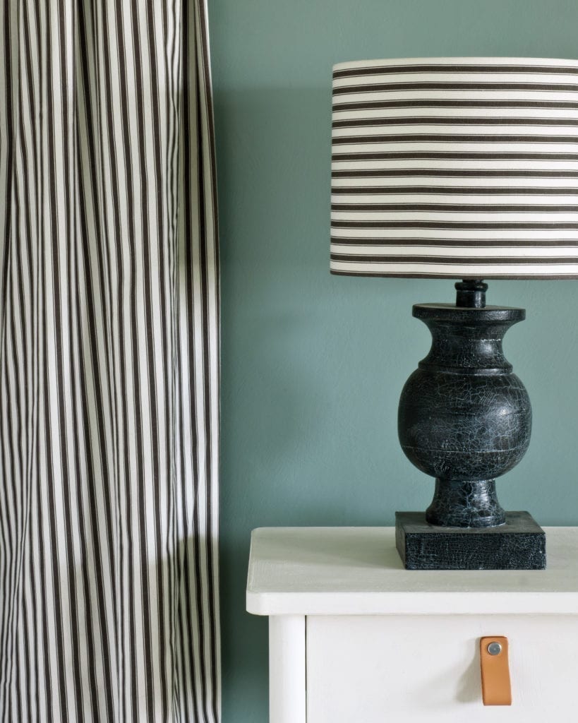 Side table painted with Chalk Paint® in Old White, a cool soft off-white, against a wall of Duck Egg Blue, with Ticking in Graphite curtain and lampshade
