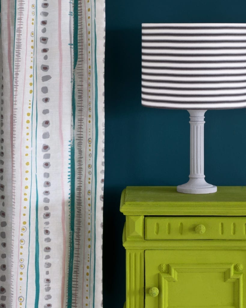 Side table painted with Chalk Paint® in Firle, a fresh, zesty and crisp green made in collaboration with Charleston Farmhouse. Against a wall of Aubusson Blue with Piano in Provence curtain and lampshade in Ticking in Graphite