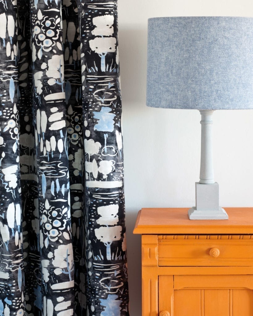 Side table painted with Chalk Paint® in Barcelona Orange, a warm and vivacious orange. Curtain in Dulcet in Graphite and Linen Union in Old Violet + Old White lampshade