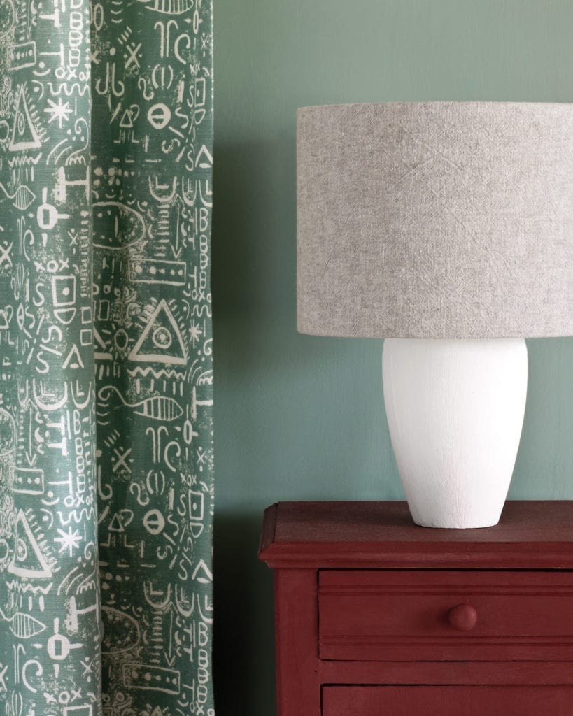 Side table painted with Chalk Paint® in Primer Red, a deep, red ochre against a wall of Duck Egg Blue. Curtain in Tacit in Duck Egg Blue and lampshade in Linen Union in Old White + French Linen