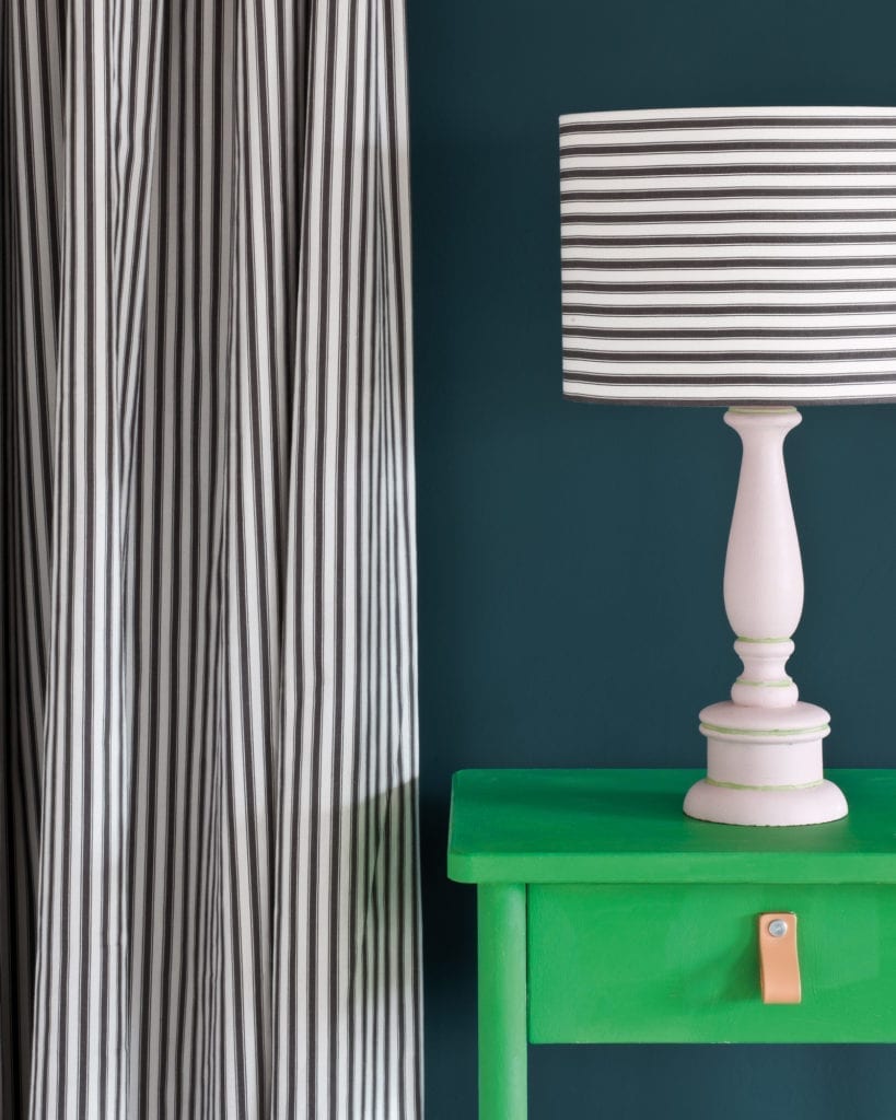 Side table painted with Chalk Paint® in Antibes Green, a bright neoclassical green against a wall of Aubusson Blue. Ticking in Graphite curtain and lampshade and lamp base in Antoinette
