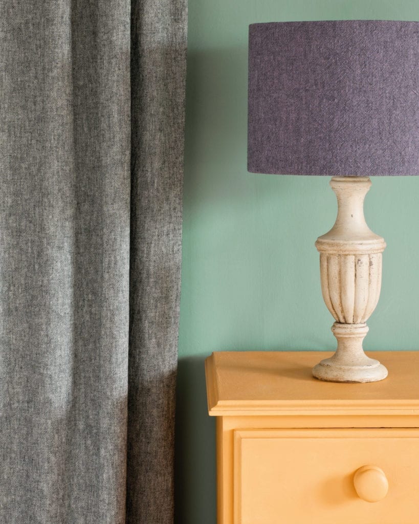 Side table painted with Chalk Paint® in Arles, a light, glowing orange-yellow against a wall of Duck Egg Blue. Linen Union in Graphite + Old White curtain and Emile + Graphite lampshade