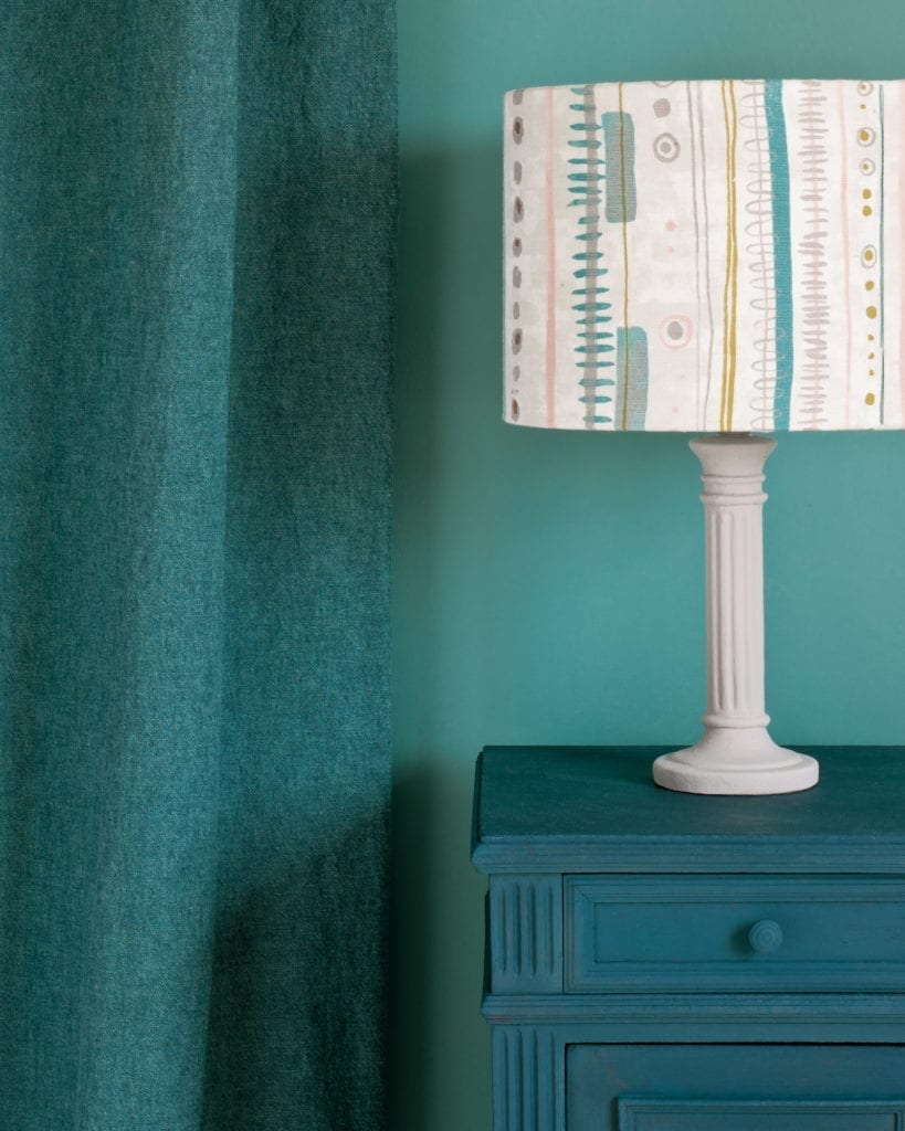 Side table painted with Chalk Paint® in Aubusson Blue, a rich dark classic green-blue teal against a wall of Provence. Curtain in Linen Union in Provence + Aubusson Blue and lampshade in Piano in Provence