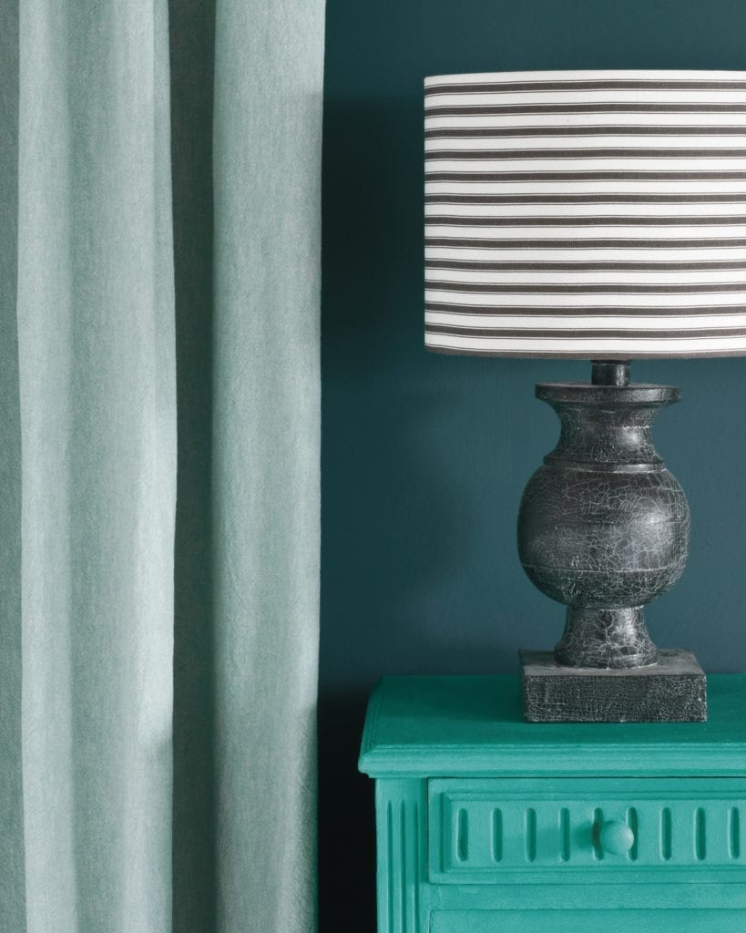 Side table painted with Chalk Paint® in Florence, a bright coppery green colour against a wall of Aubusson Blue. Linen Union in Provence + Old White curtain and Ticking in Graphite lampshade