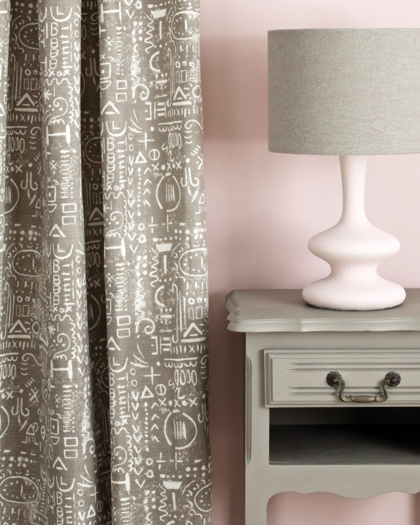 Side table painted with Chalk Paint® in French Linen, cool neutral khaki grey beige against a light pink wall of Antoinette. Curtain in Tacit in French Linen and lampshade in Linen Union in Coco + Duck Egg Blue