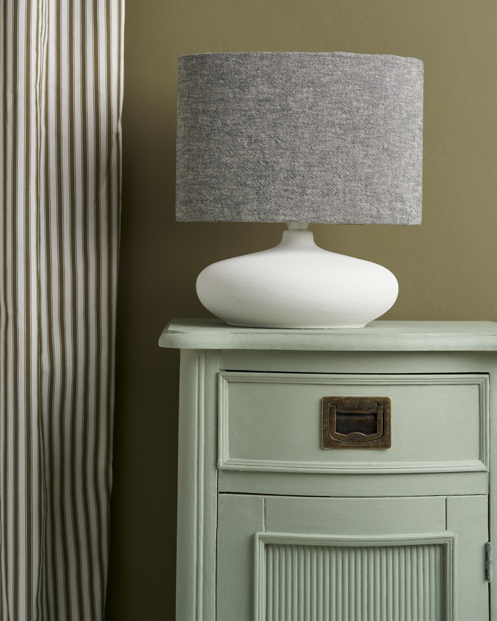 Close Up Side Table Painted in Coolabah Green Chalk Paint and Staged against Olive Wall Paint Background and Featuring Fabric Lamp and Curtains